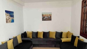 Una sala de estar con un sofá modular, dos cuadros en las paredes y una puerta de madera.