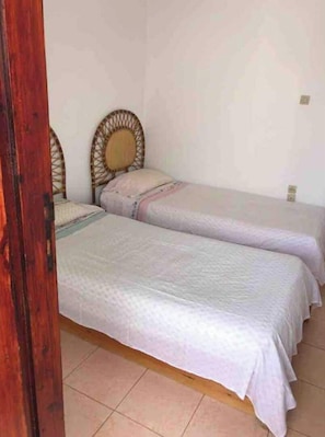 Une chambre avec deux lits simples, chacun doté d’une tête de lit en bois et d’une couvre-lit blanche.