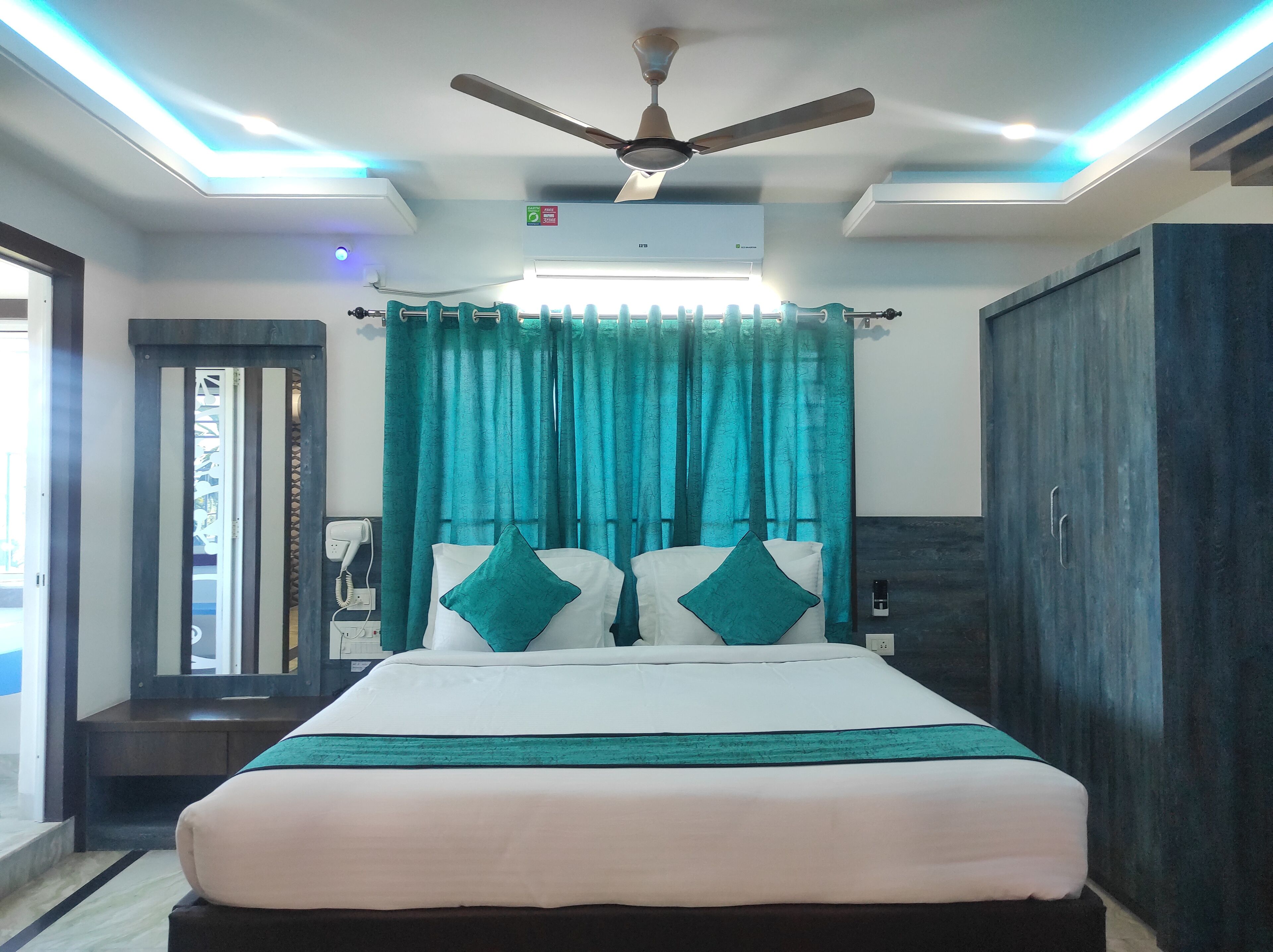 A hotel room with a bed, teal curtains, a ceiling fan, and an air conditioning unit.
