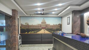 Uma área de recepção com piso de mármore, balcão de atendimento, ventilador de teto e um mural de um edifício.