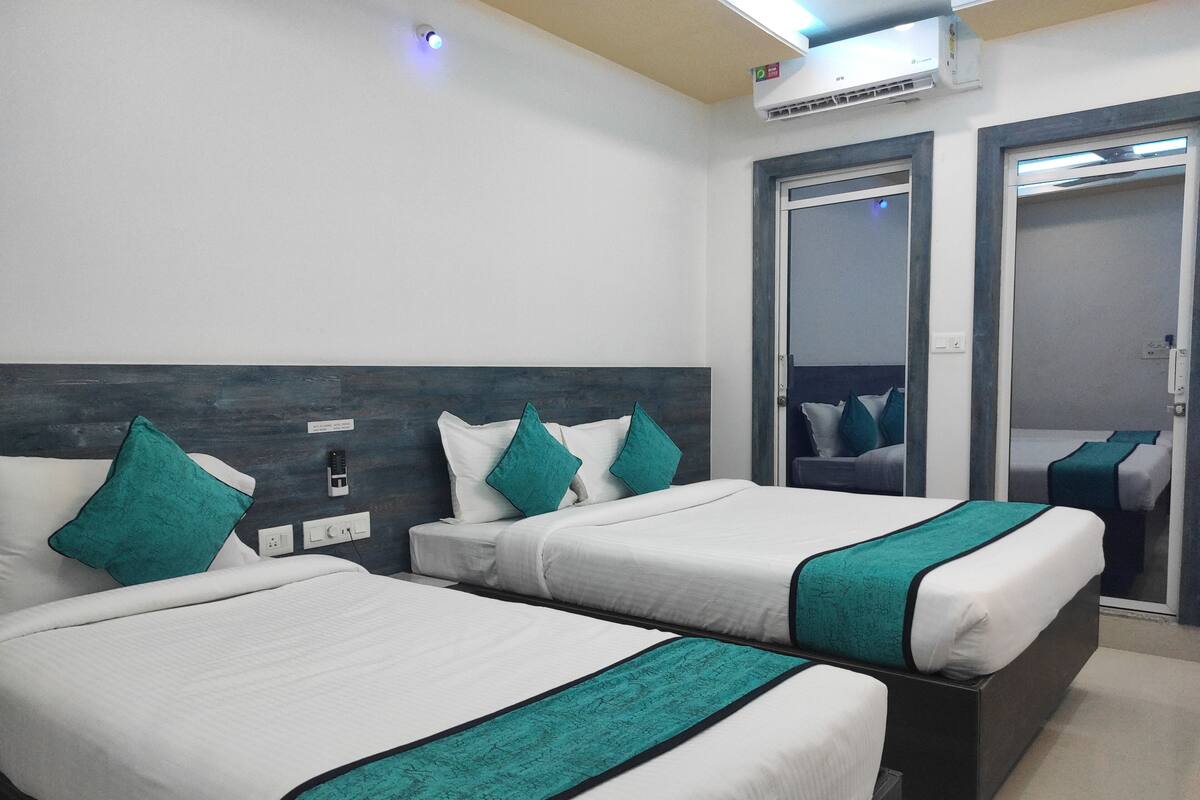 Ein Hotelzimmer mit zwei Betten, einem dunklen Kopfteil, weißer Bettwäsche, türkisfarbenen Zierkissen, einem Spiegel und einer Decken-Klimaanlage.
