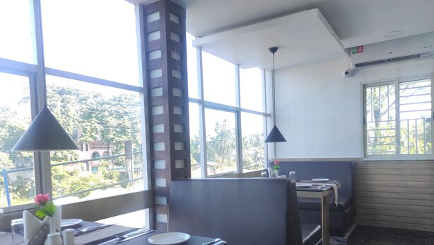 Restaurante com janelas altas, varanda e vista para vegetação. Mesas montadas com pratos, talheres e um vaso de flores.