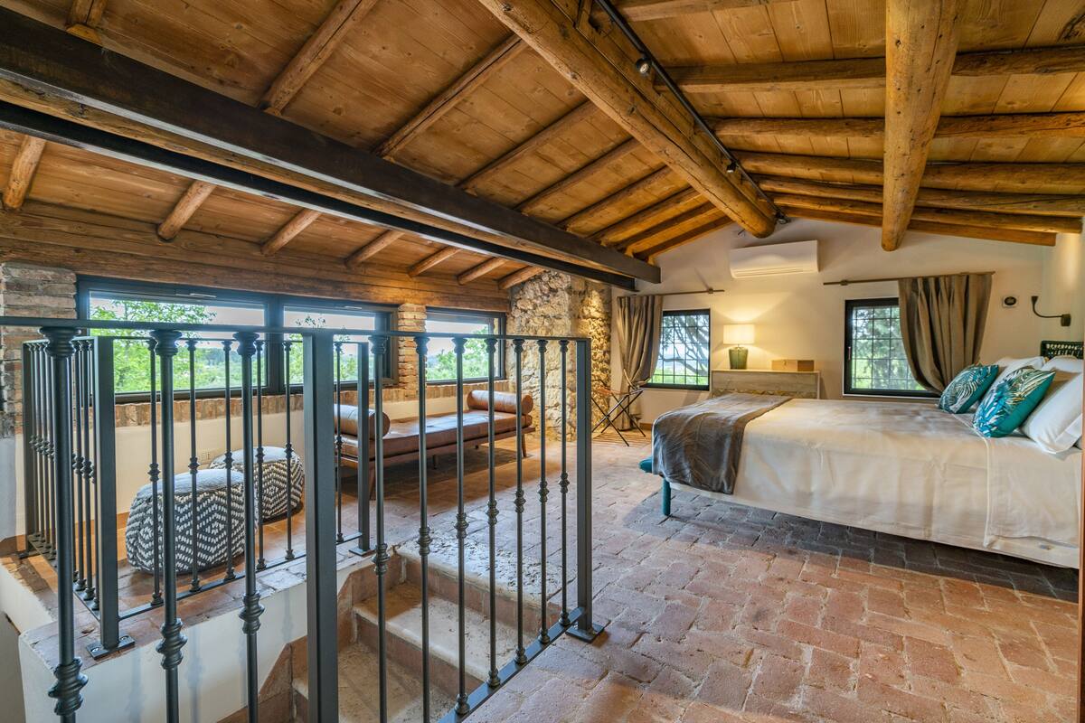 A bedroom with a large bed, a stone wall, and a balcony with a railing.