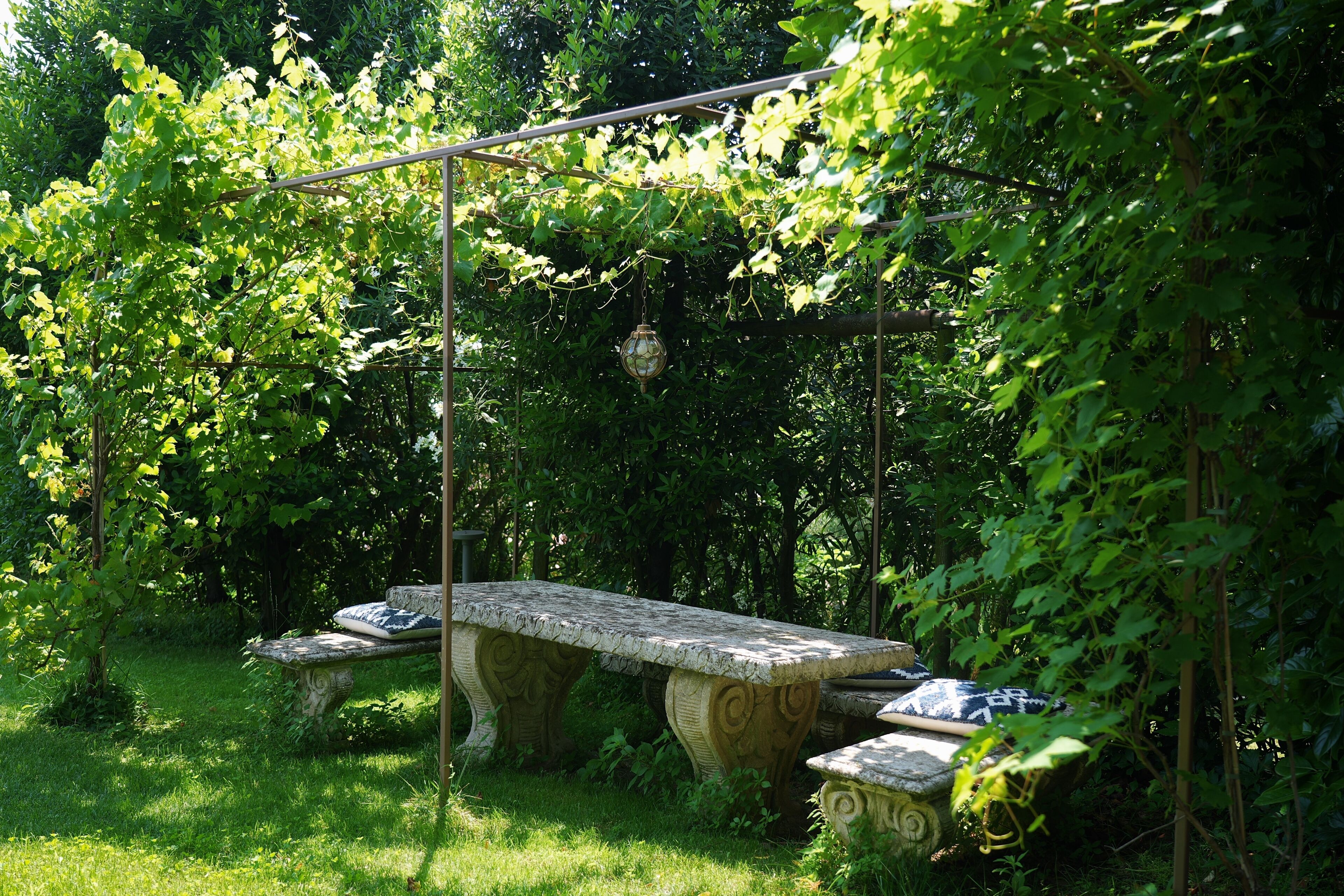 Ein Garten mit einer Steinsitzbank und einer Pergola.