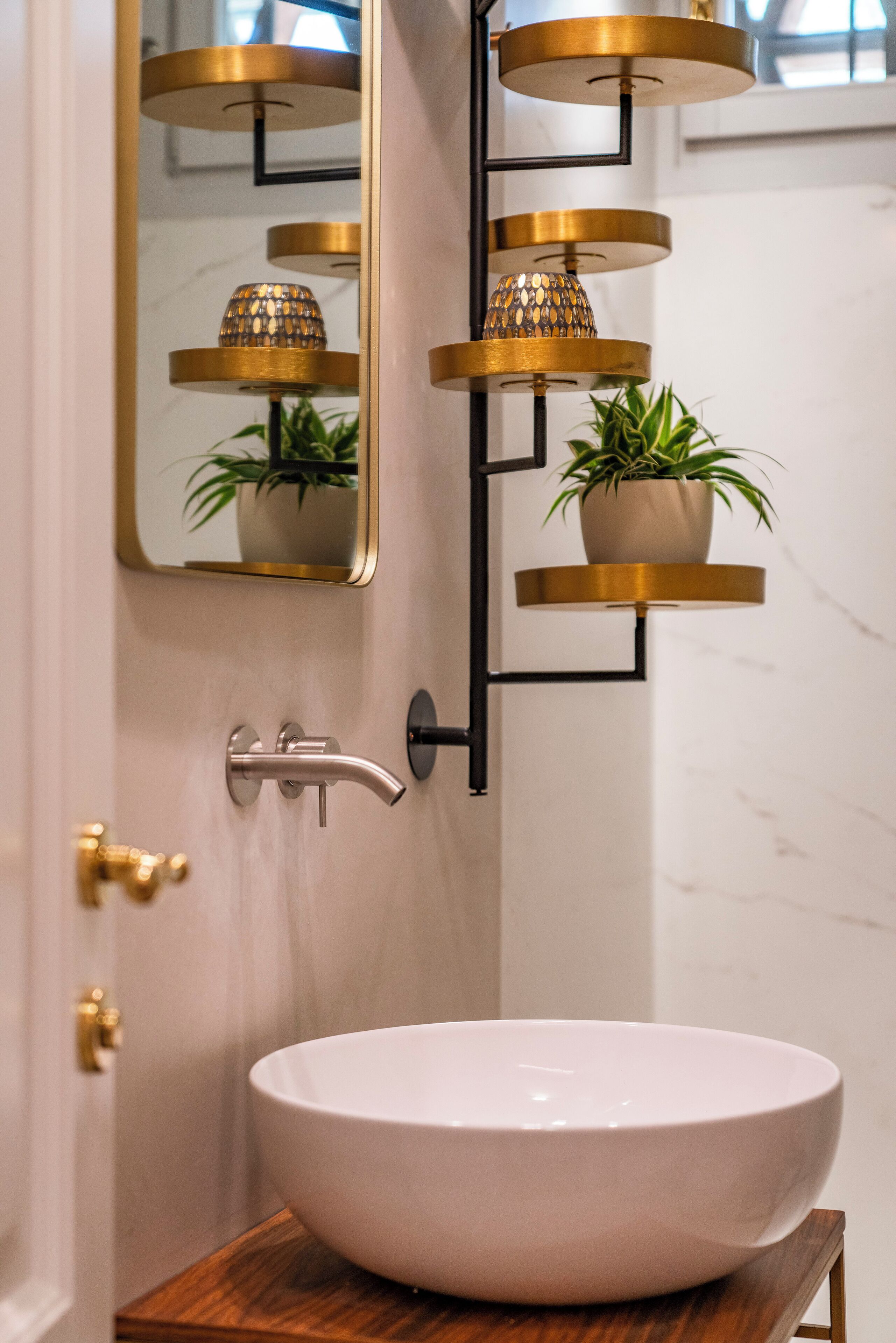 Un baño con lavamanos blanco, detalles dorados y un espejo.