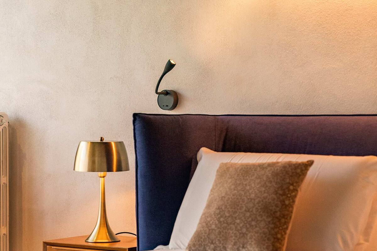 A neatly made bed with a dark headboard, a bedside lamp, and a wall-mounted light fixture.