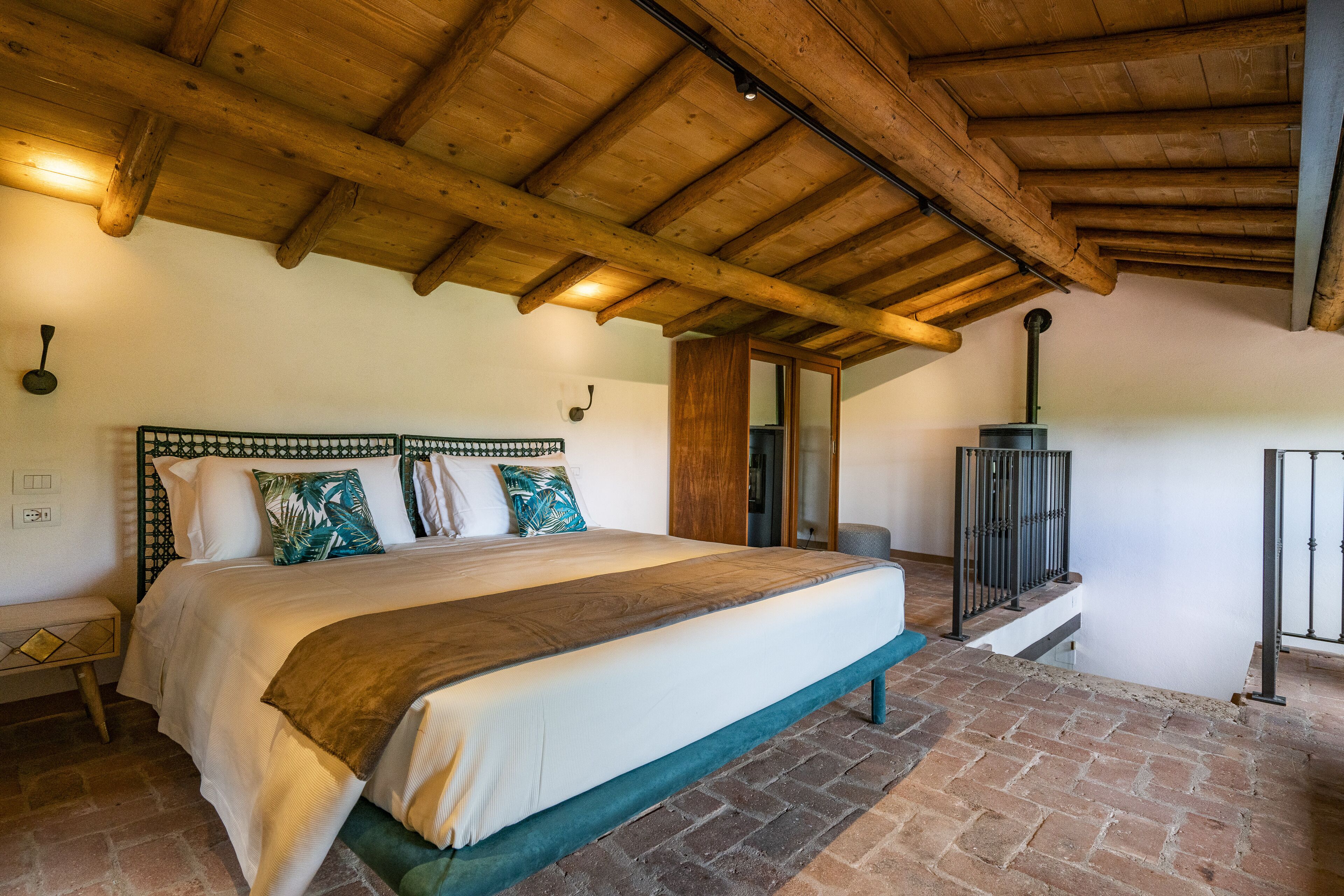 Ein Schlafzimmer mit einem großen Bett, Holzbalkendecke, Ziegelboden und Kamin.