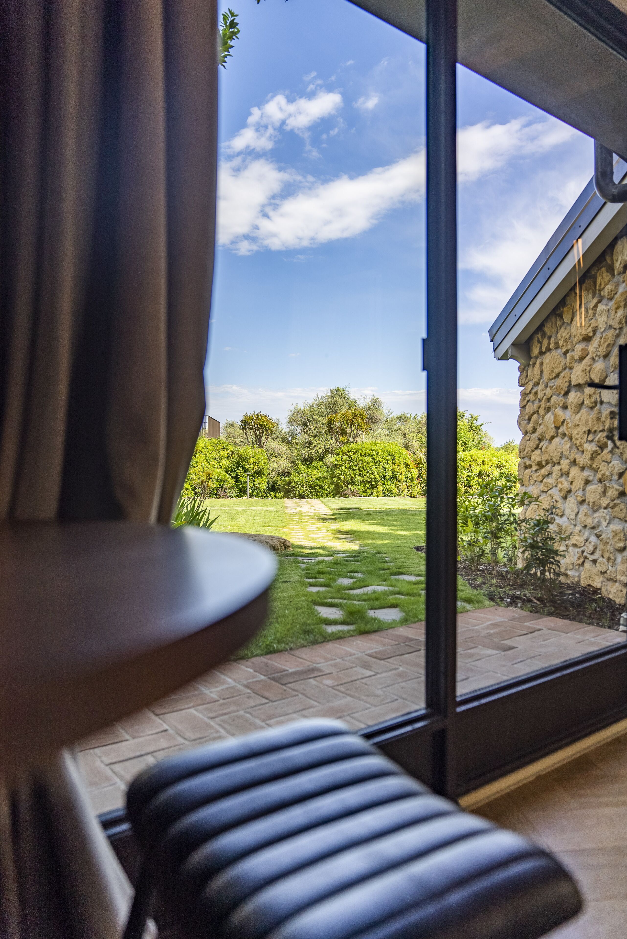 A room with a large window overlooking a garden and a stone building.