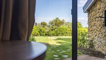A room with a large window overlooking a garden and a stone building.