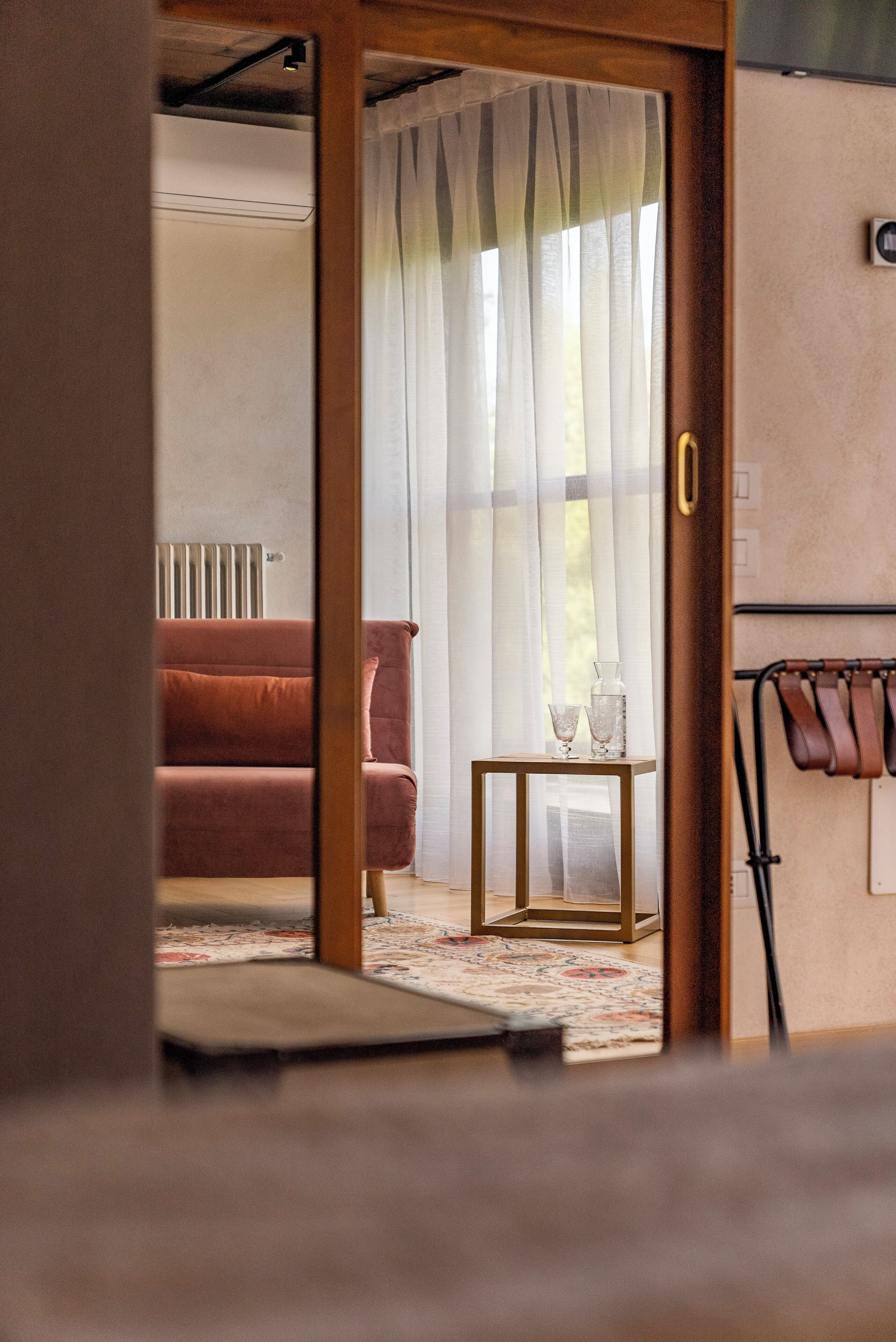 Ein Zimmer mit einer raumhohen Schiebetür aus Holz, die in einen Wohnbereich mit einer Couch, einem kleinen Tisch mit einer Vase und einem Heizkörper führt.