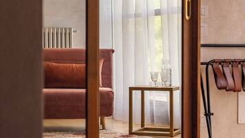 A room with a wooden-framed sliding door leading to a living area with a sofa, a small table with a vase, and a radiator.