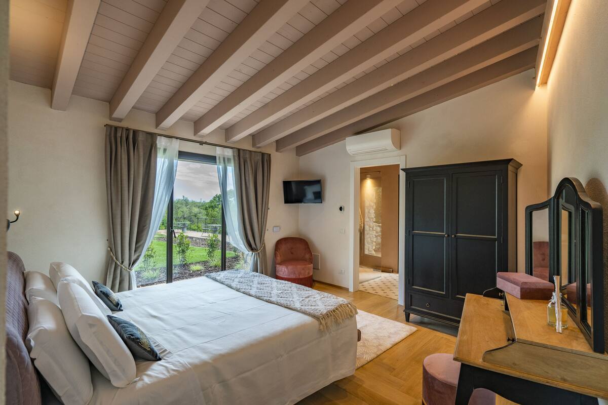 A bedroom with a large bed, a wooden desk, a chair, a wardrobe, and a TV.