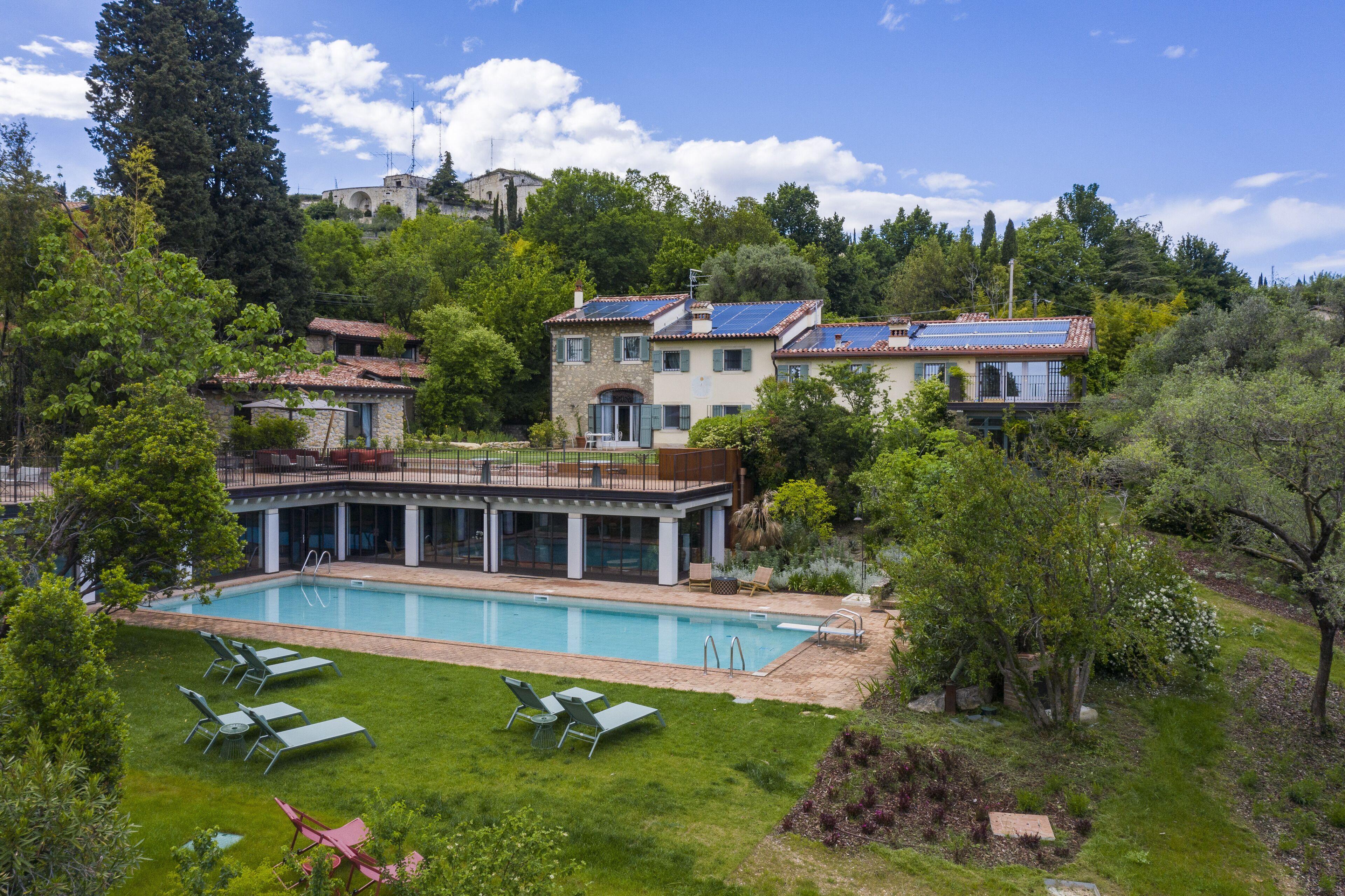 Una piscina con sillas de descanso, un edificio de piedra y una ladera cubierta de bosque.