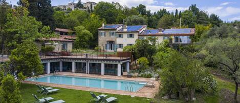 Una piscina con sillas de descanso, un edificio de piedra y una ladera cubierta de bosque.