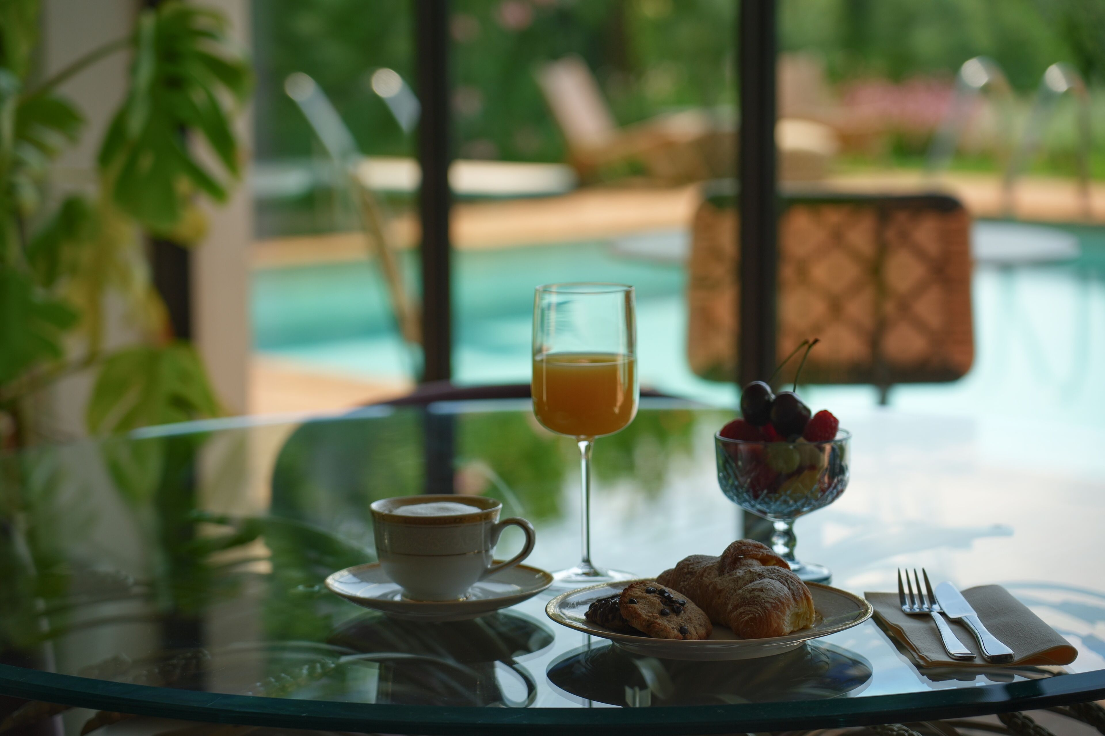 Una mesa de desayuno con una taza de café, un vaso de jugo de naranja, un plato de croissants y un bol de fruta.