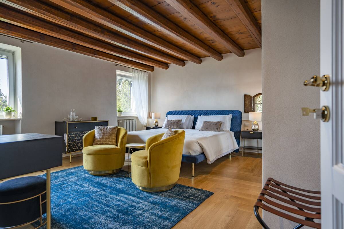 A bedroom with a bed, two yellow armchairs, a desk, and a window.