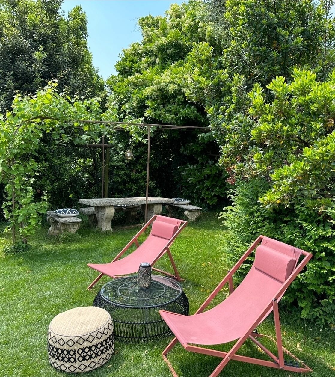 Un jardín con dos sillones rojos, una mesa redonda y un banco de piedra.