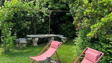 Un jardín con dos sillones rojos, una mesa redonda y un banco de piedra.