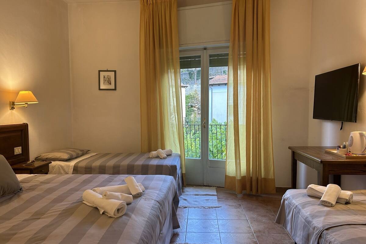 A hotel room with two beds, a desk, a television, and a window with curtains.