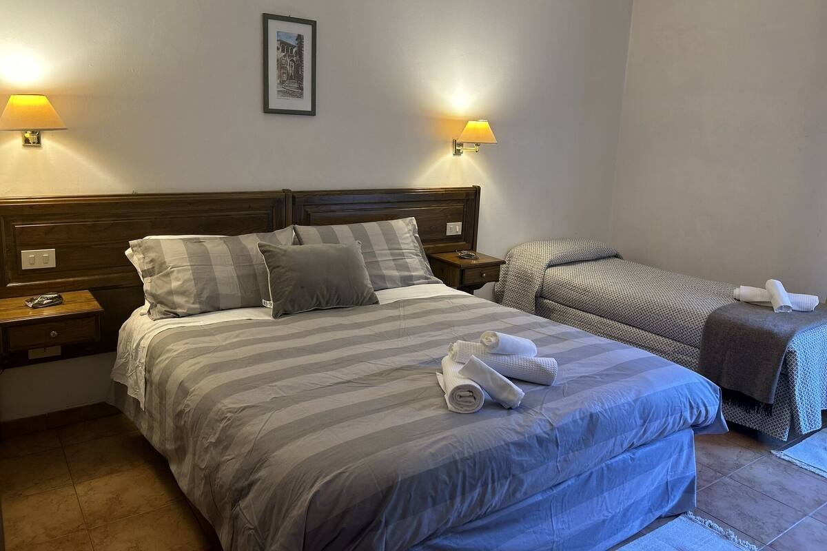 A hotel room with two beds, a headboard, bedside lamps, a framed picture on the wall, and a small table with a lamp.