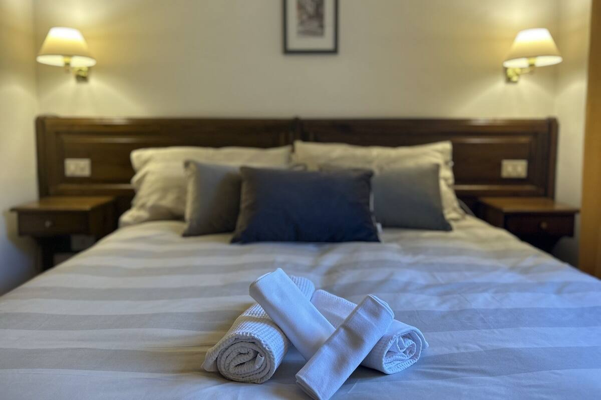 A neatly made bed with white and grey linens, two bedside lamps, and a framed picture on the wall.