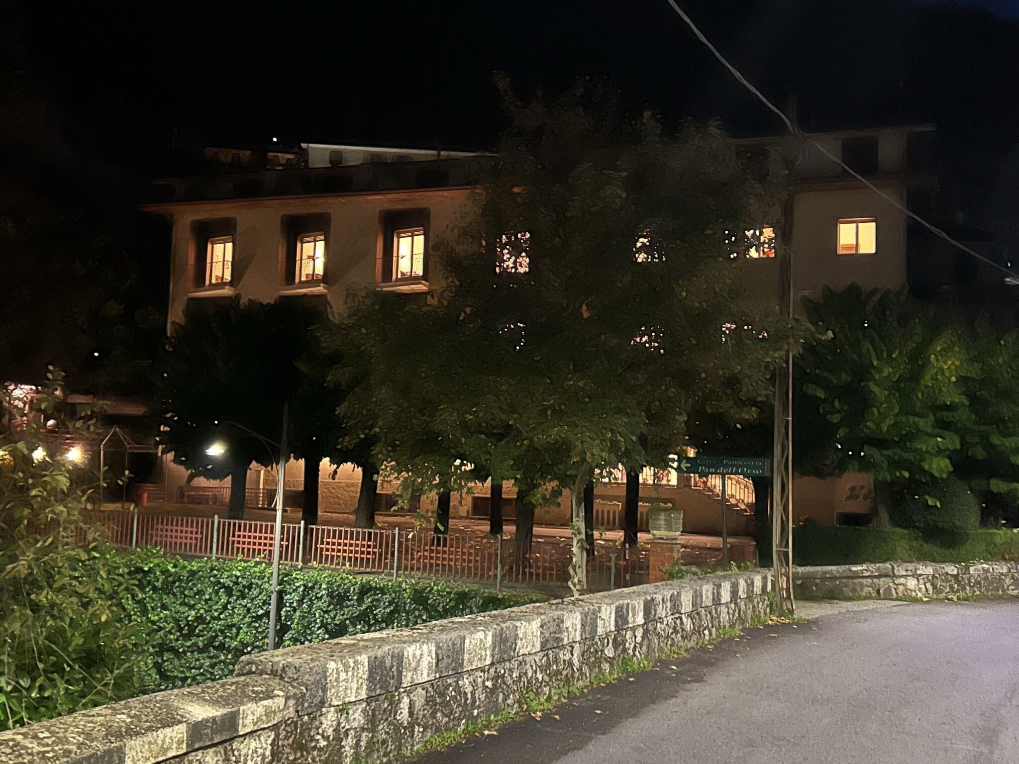 Une vue nocturne d’un bâtiment doté de nombreuses fenêtres, d’un mur en pierre et d’une route pavée.