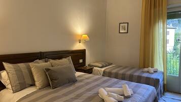 Une chambre d’hôtel avec deux lits, une table de chevet, une lampe, un tableau encadré et une vue sur la verdure à l’extérieur.