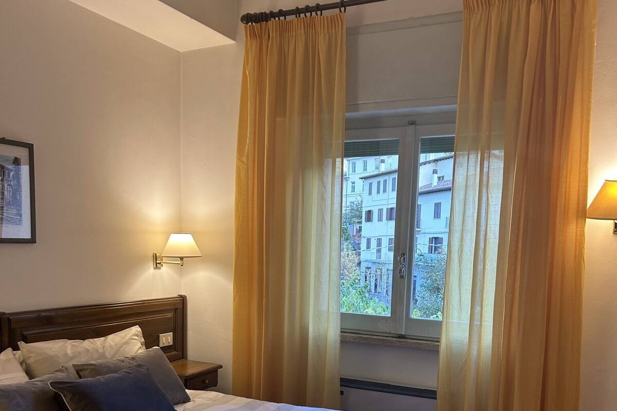 A neatly made bed with pillows, a bedside lamp, and a window with curtains.
