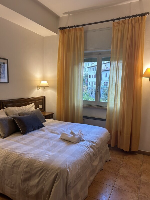 A neatly made bed with pillows, a bedside lamp, and a window with curtains. - Le Focette Dell'Orso (Scanno)