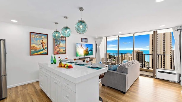 Eine moderne Küche mit einer zentralen Kochinsel, ein Essbereich mit einer Couch und ein Balkon mit Blick auf die Stadt.