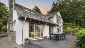 A house with a stone exterior, a large patio with a table and chairs, and a view of the surrounding greenery. - Barakat Lakes Escape (Ambleside)