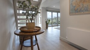 A modern interior with a wooden floor, a wicker table with a plant, and a framed map on the wall. - Barakat Lakes Escape (Ambleside)