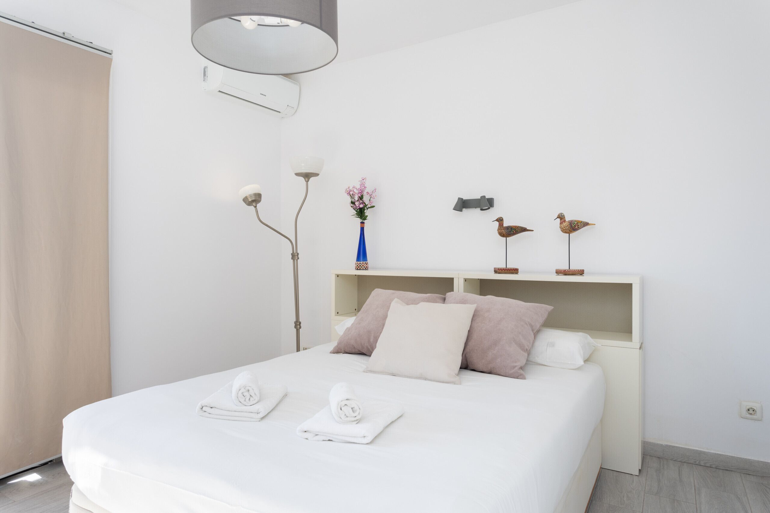 Une chambre d’hôtel moderne avec un grand lit, une table de chevet, un vase de fleurs et des œuvres d’art décoratives au mur.