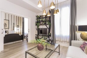 Ein modernes Wohnzimmer mit einer Couch, einem Couchtisch mit einer Vase, einem Fernseher und einem Bücherregal mit Pflanzen.