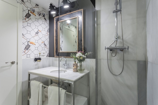 A bathroom with a glass-enclosed shower, a white sink, a mirror with a wooden frame, and a wall with a hexagonal tile pattern.