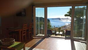 Un comedor con mesa y sillas, vistas al mar a través de amplios ventanales y suelo de madera.