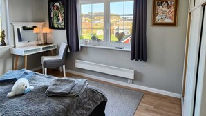 Un dormitorio con cama, escritorio, silla, radiador y ventana con cortinas.