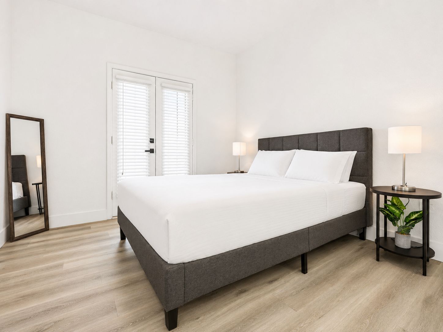 Un dormitorio moderno con una cama grande, mesitas de noche, un espejo y una planta en maceta.