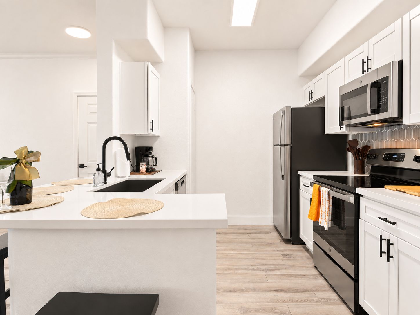 A modern kitchen with white cabinetry, a central island, a stainless steel refrigerator, and an oven.