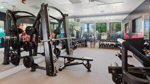 A gym with weightlifting equipment, mirrors, and a ceiling fan.