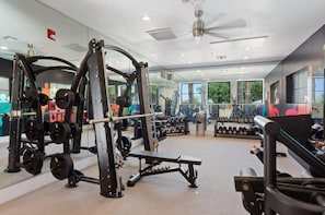Une salle de sport équipée de matériel de musculation, de miroirs et d’un ventilateur au plafond.