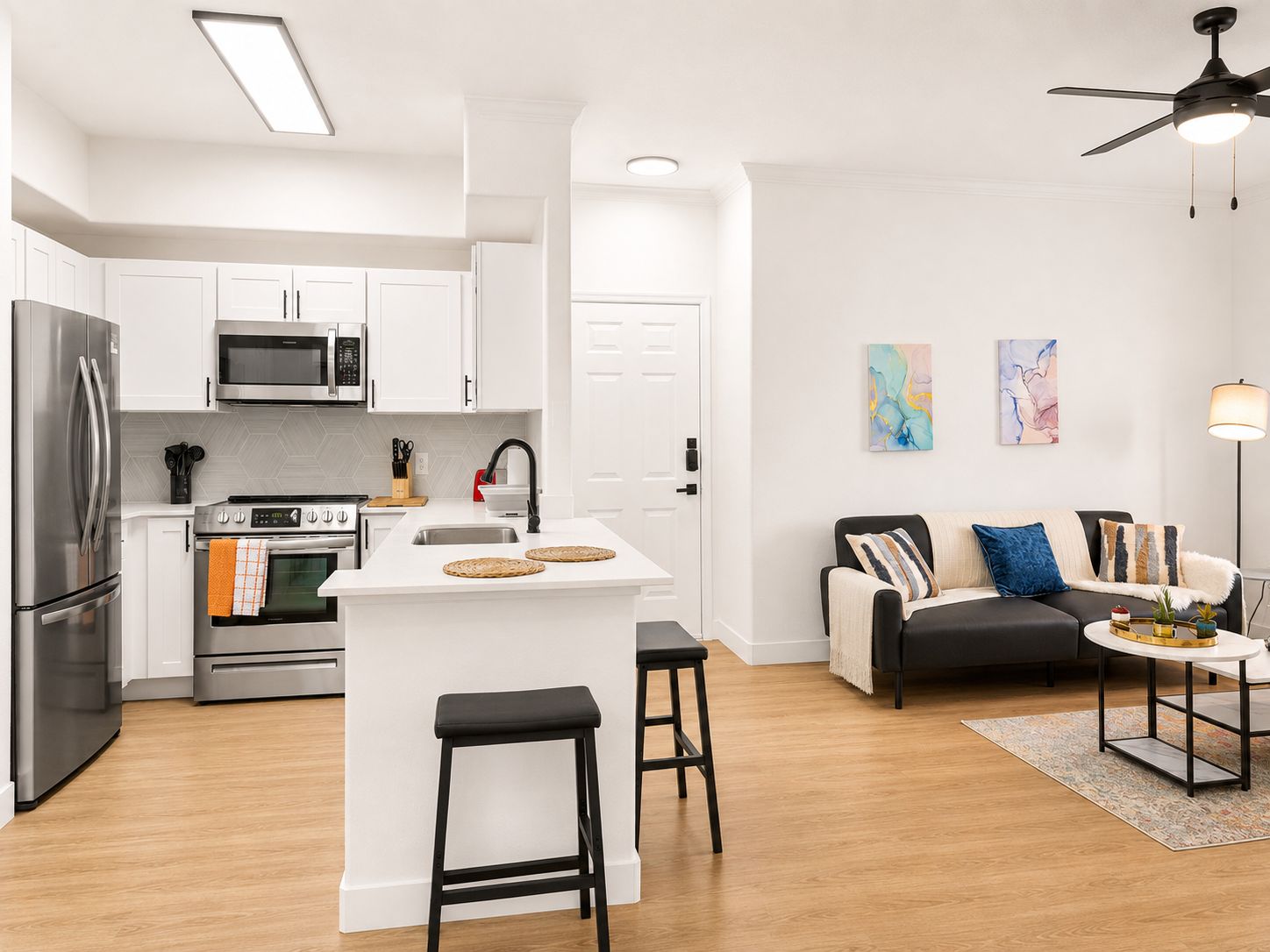 A modern kitchen with white cabinetry, stainless steel appliances, and a central island with stools.