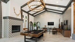 A spacious living area with a pool table, a fireplace, and a modern chandelier. - CozySuites at Chandler (Chandler)