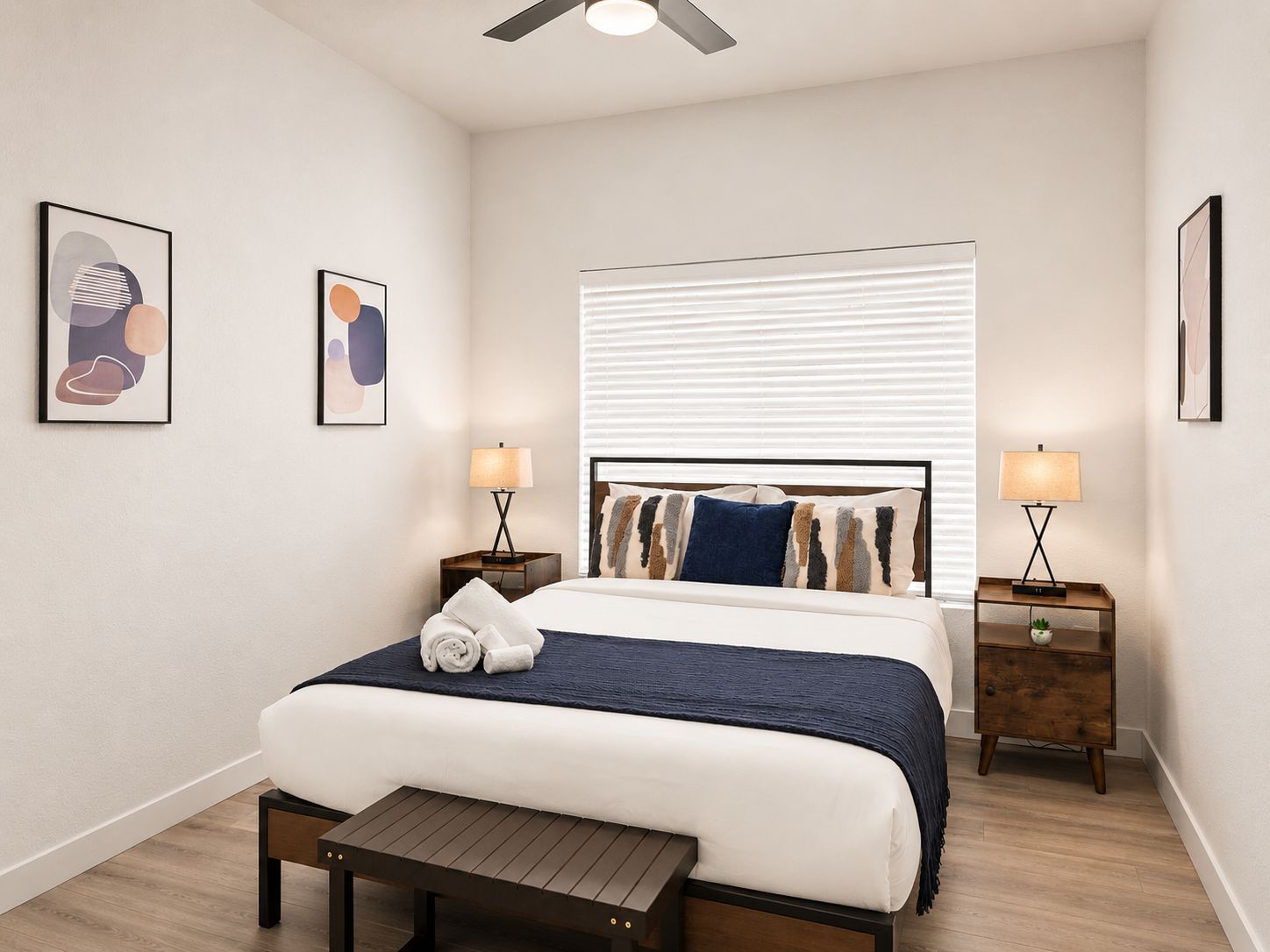 A neatly arranged bedroom with a bed, bedside tables, and artwork on the walls.
