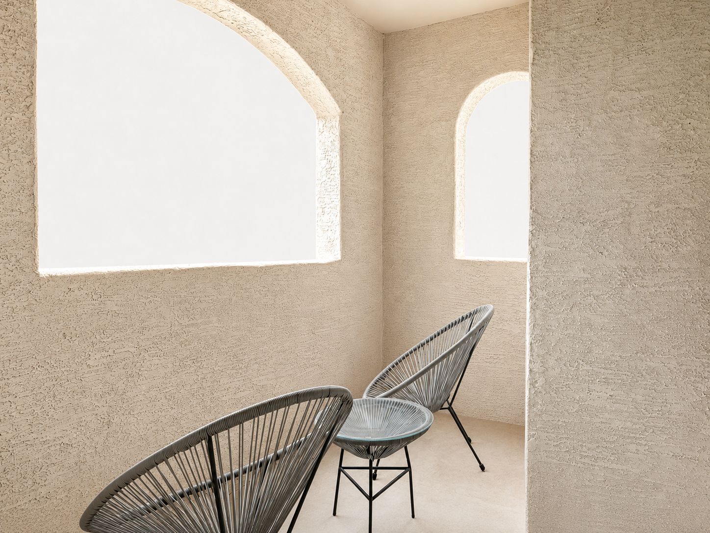 A room with textured walls, two chairs, and two arched windows.