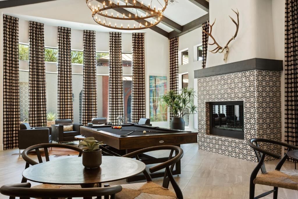 A modern living room with a pool table, comfortable seating, a fireplace, and a large window with curtains.