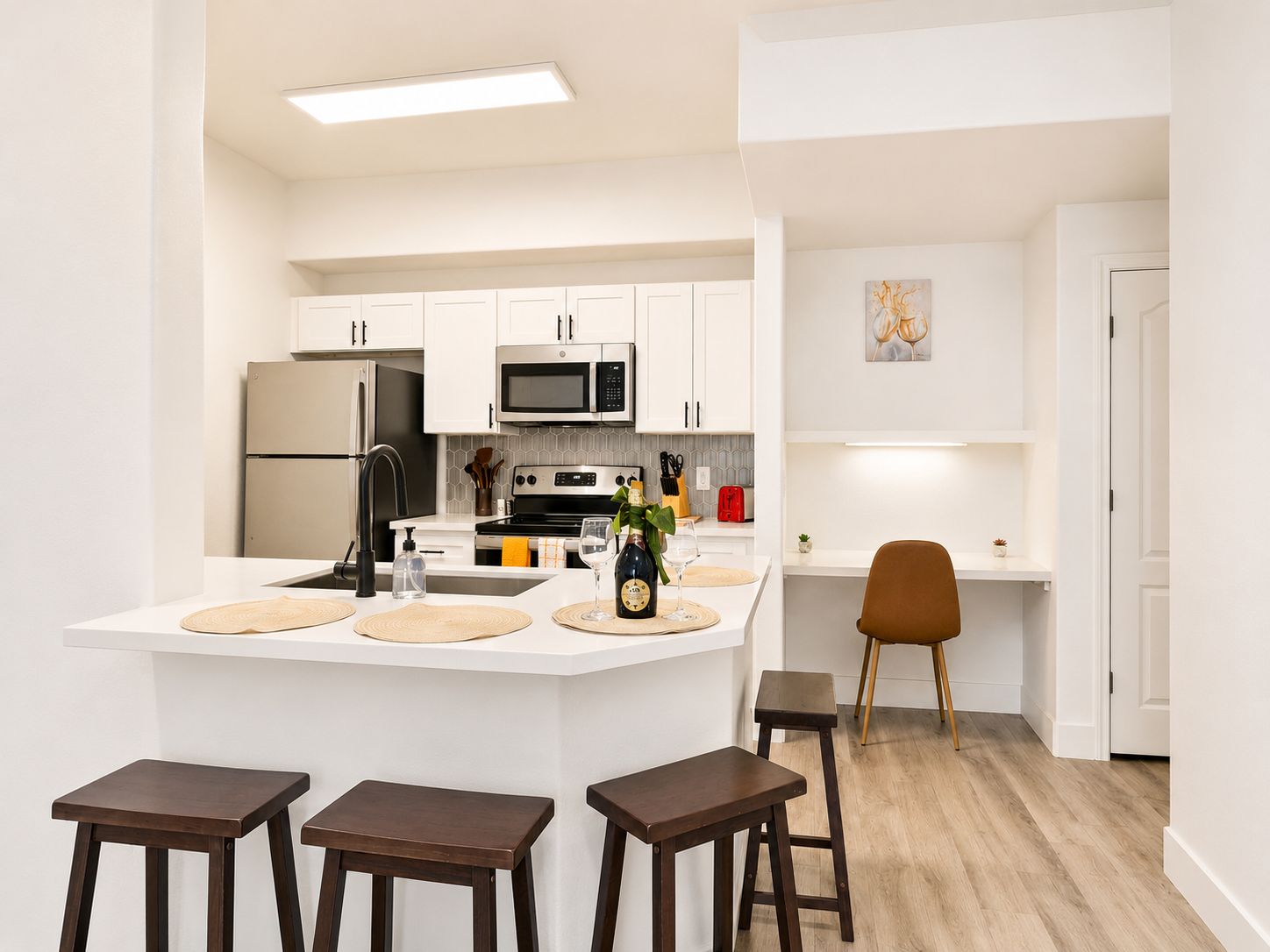 A modern kitchen with white cabinetry, a central island with stools, a microwave, and a refrigerator.