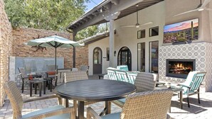 An outdoor patio with a round table and wicker chairs, a stone wall, and a fireplace. - CozySuites at Chandler (Chandler)