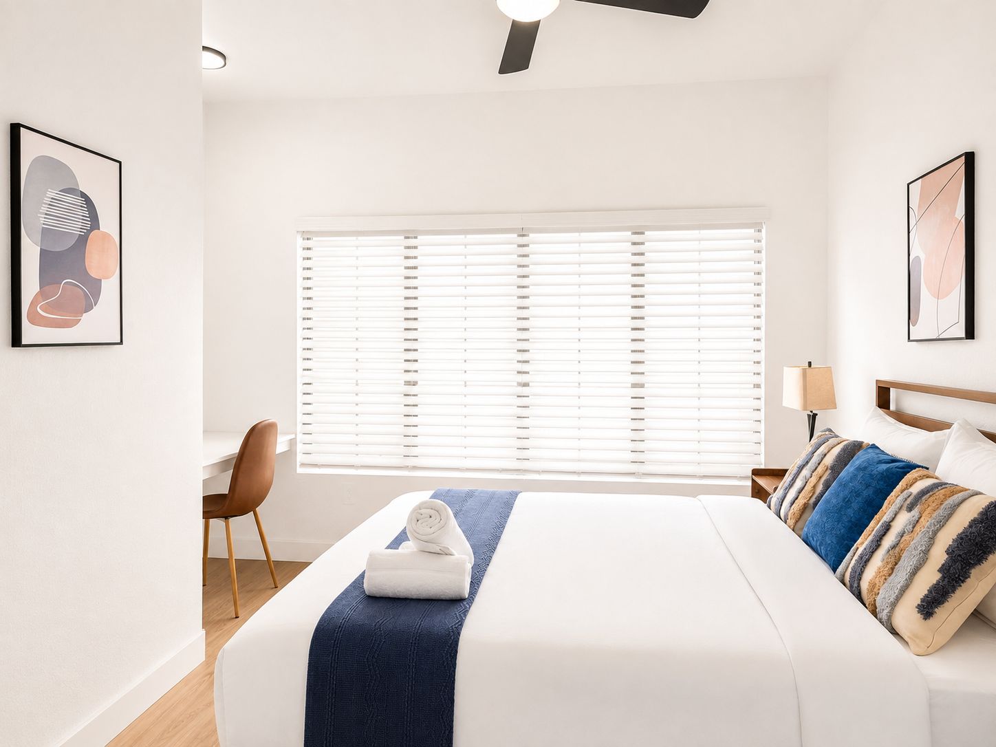 Quarto de hotel com cama, escrivaninha e janela com persianas.