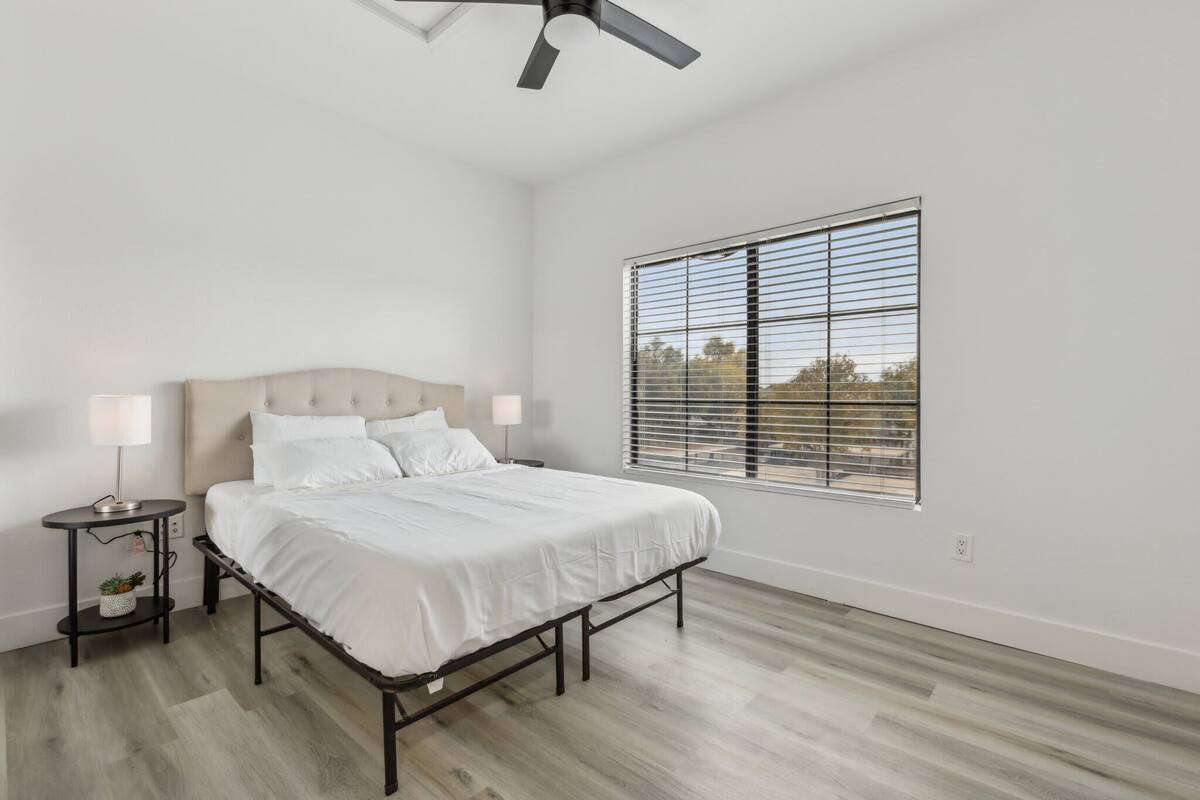 A bedroom with a bed, bedside tables, a ceiling fan, and a window with blinds.
